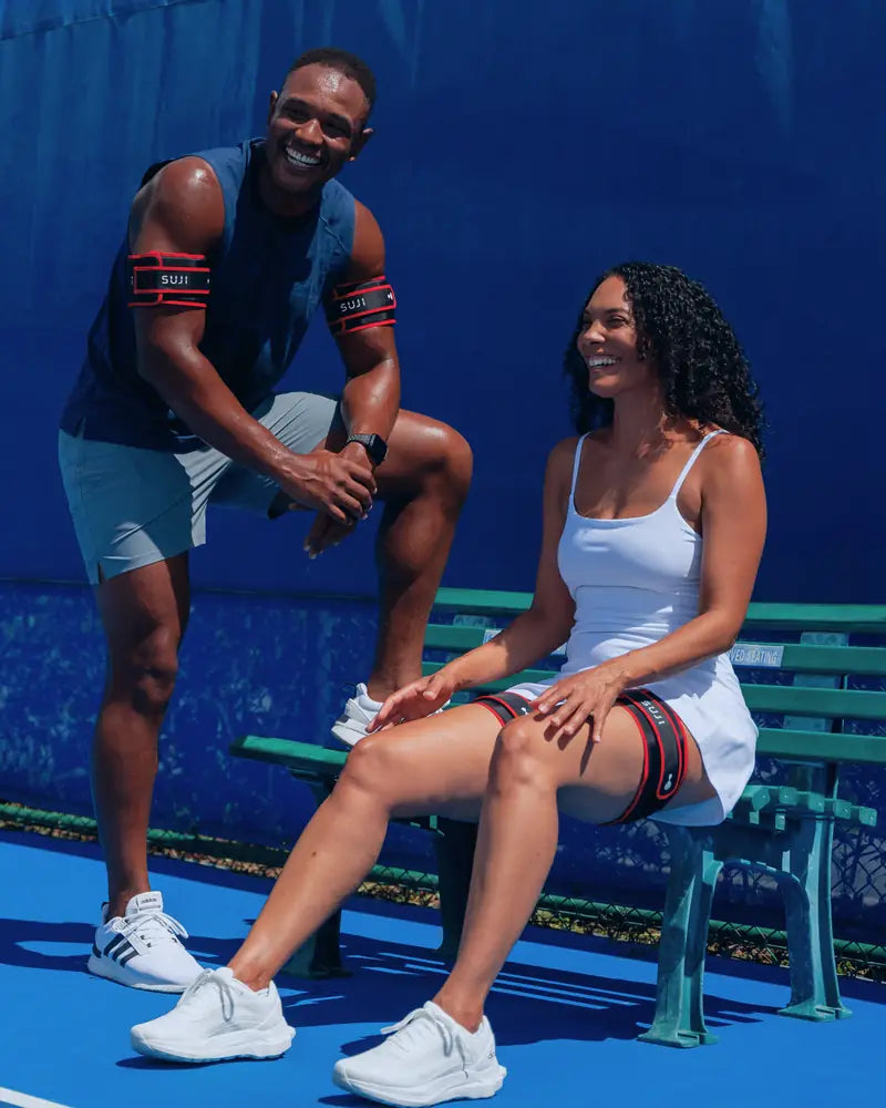 Two people wearing Suji cuffs on their arms and legs, seated courtside.